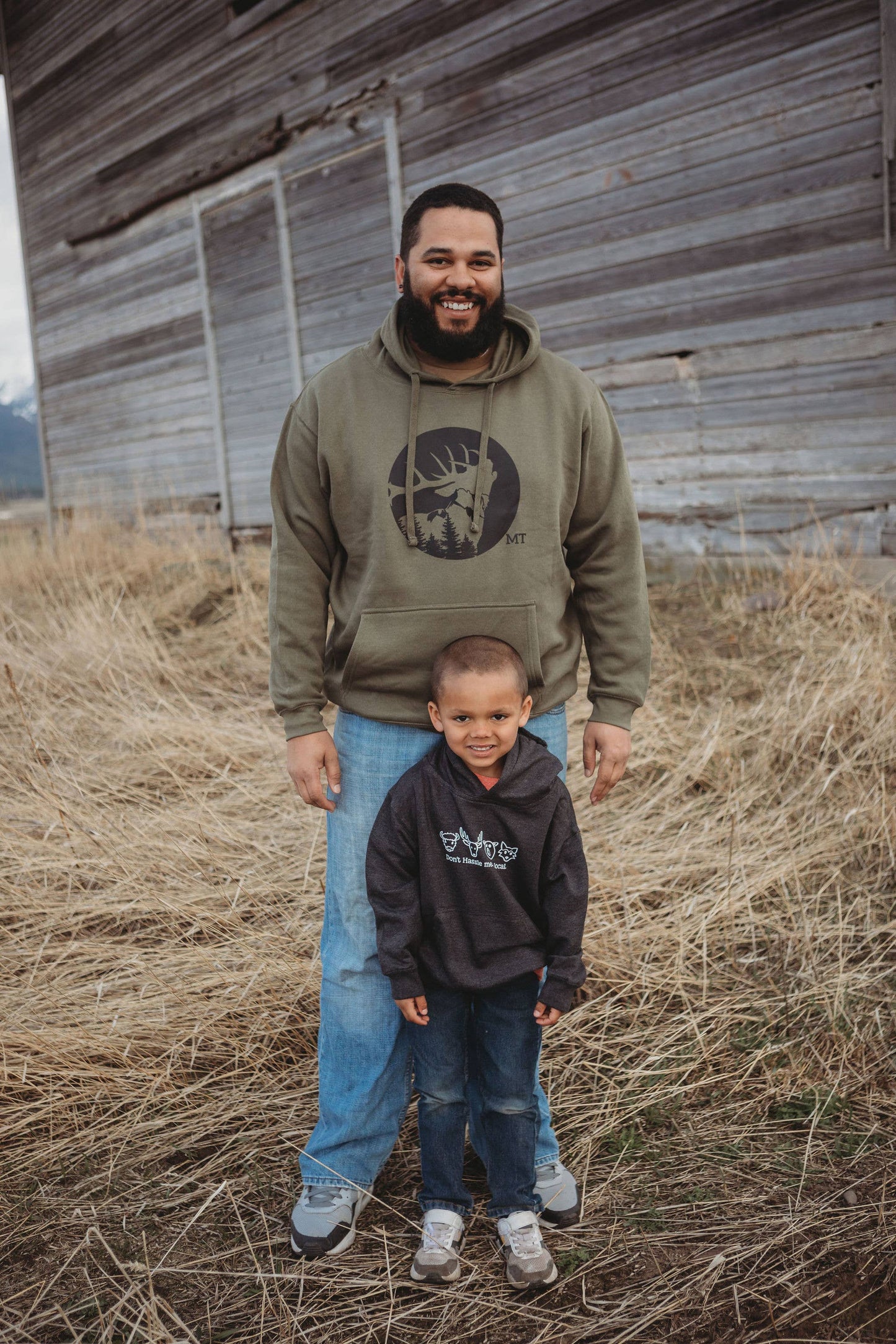 Two people wearing hoodies standing in front of a wooden building.