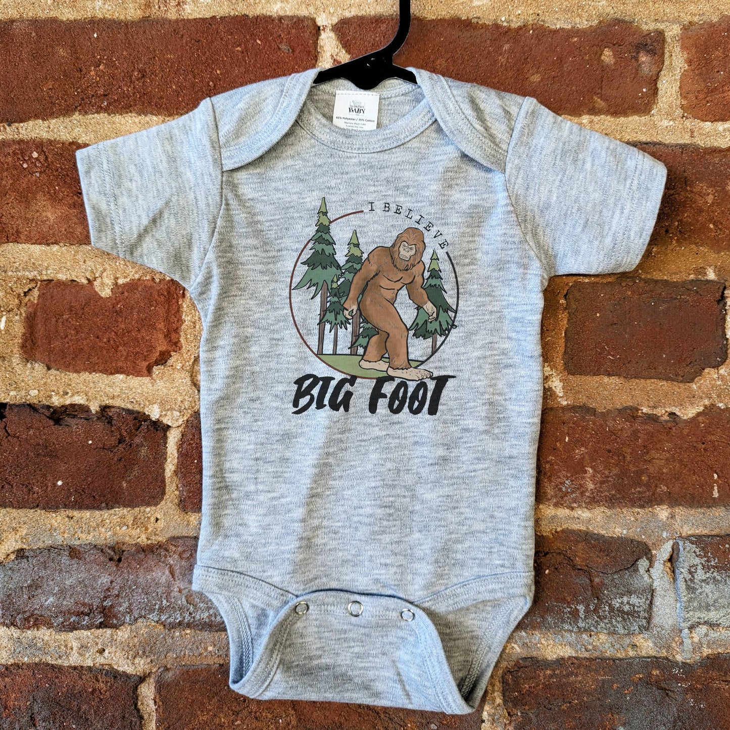 Gray baby onesie with Bigfoot graphic on a brick wall