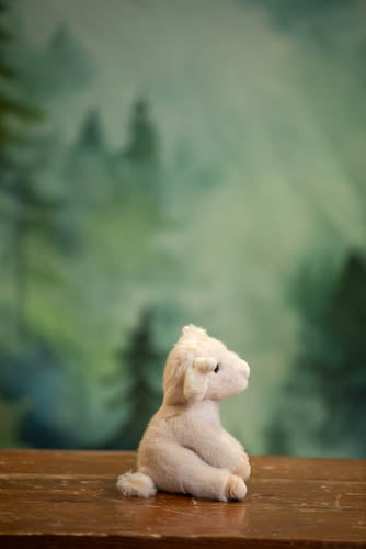 Small plush poodle toy on a wooden surface with a blurred green background