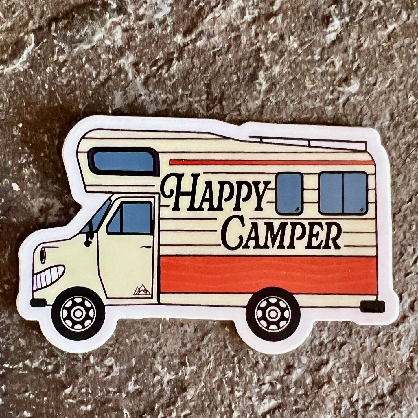 Sticker of a camper van with 'Happy Camper' text on a textured surface