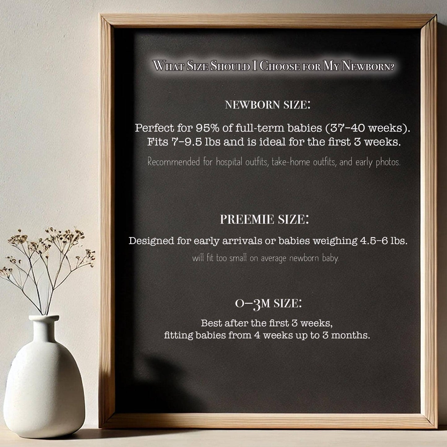 Framed chart detailing baby size information on a neutral background with a vase.