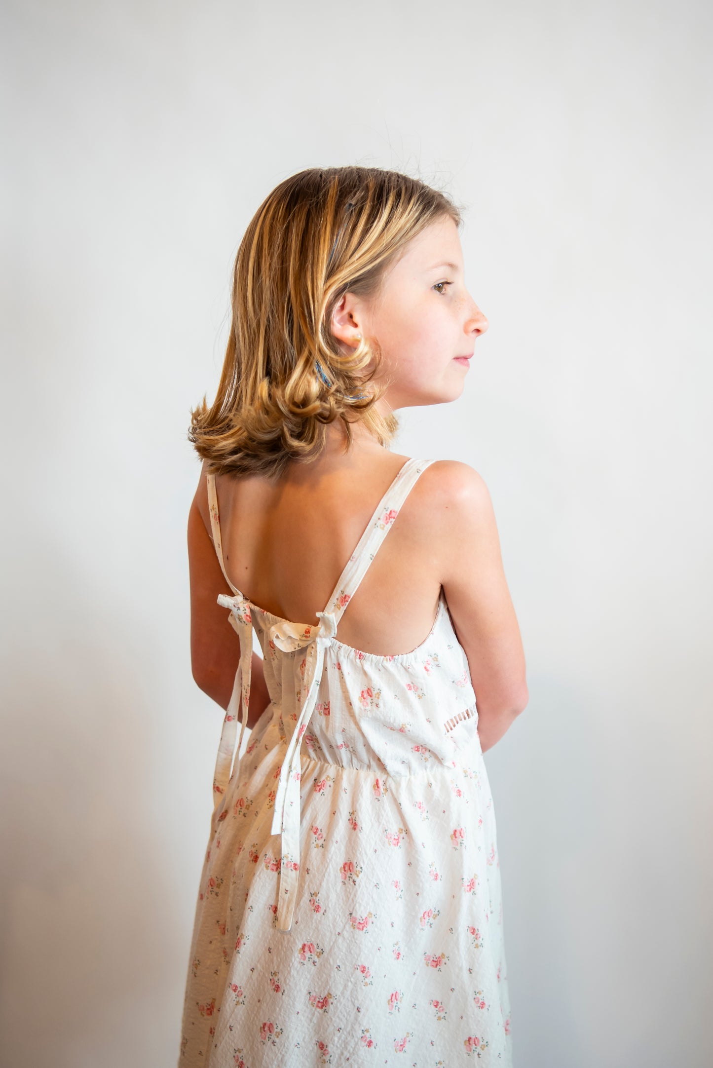 tween wearing a white sundress with bow straps and small pink flowers on it