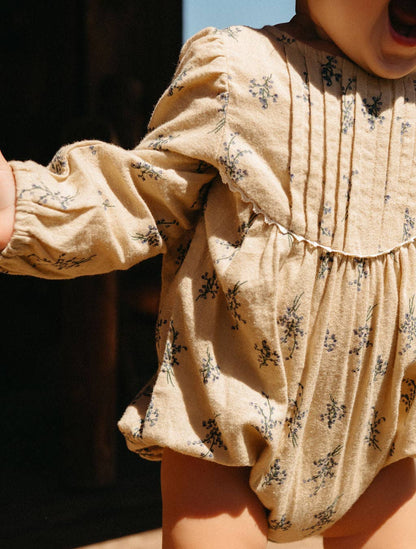 Close-up of a child wearing a beige floral romper with sunlight casting shadows.
