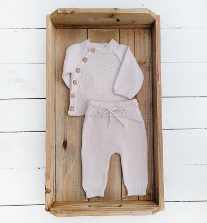 Knitted baby outfit with cardigan and pants in a wooden box on a white wooden floor.