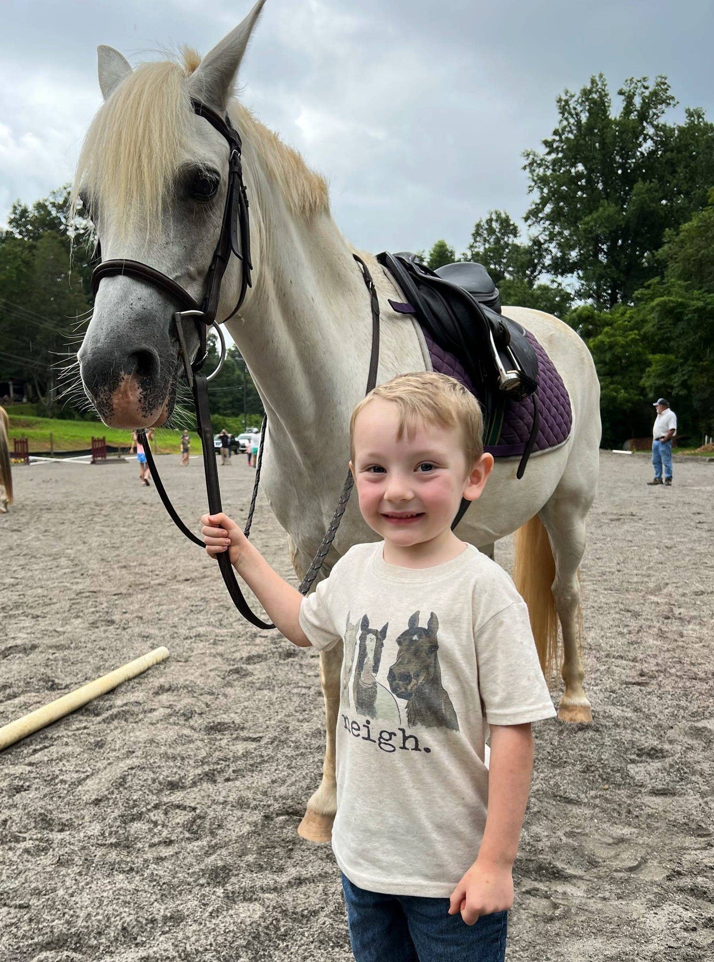 Child standing next to a horse in an outdoor equestrian setting