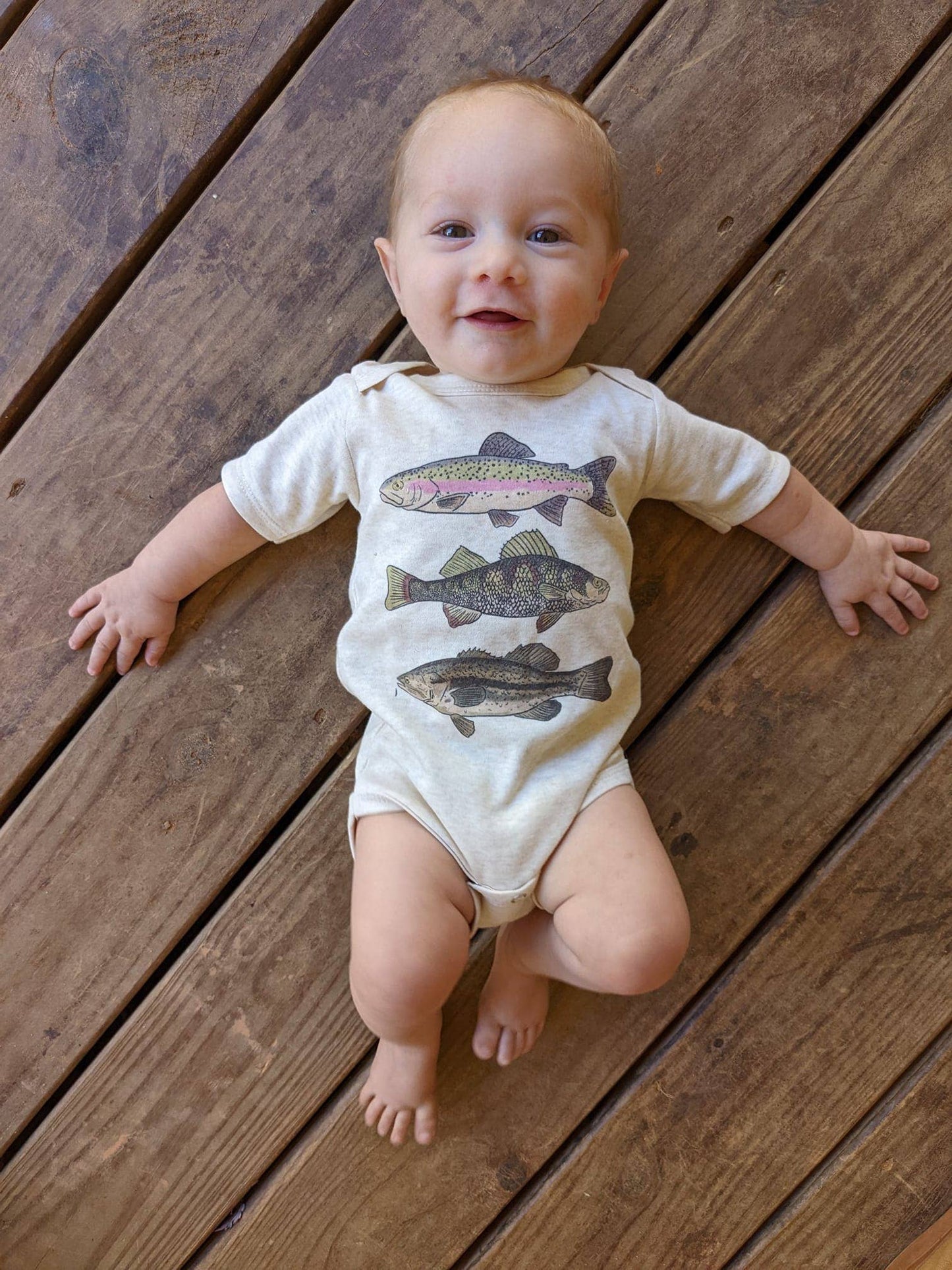 Baby wearing a onesie with fish illustrations on a wooden floor