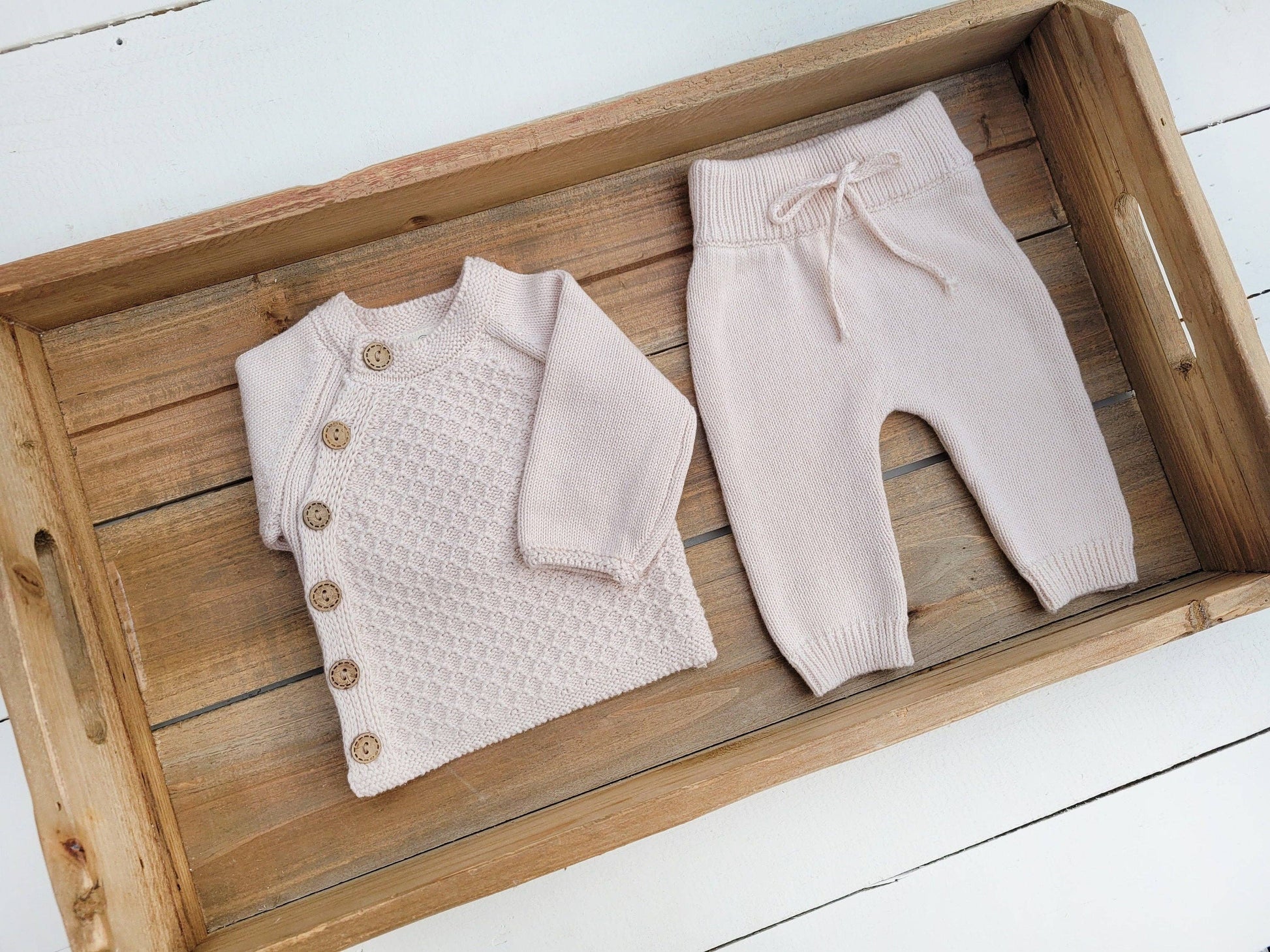 Baby sweater and pants set on a wooden tray with a white background