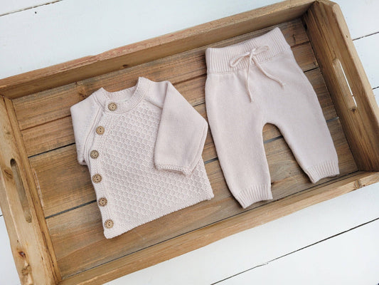 Baby sweater and pants set on a wooden tray with a white background