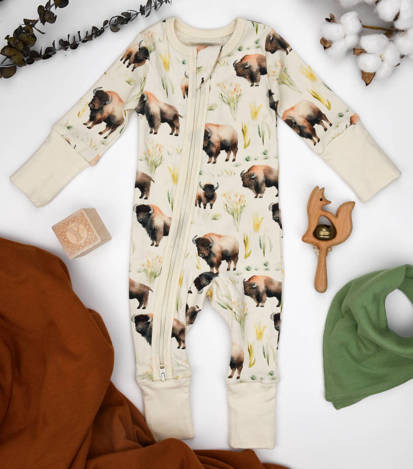 Baby romper with animal print surrounded by baby items on a white background