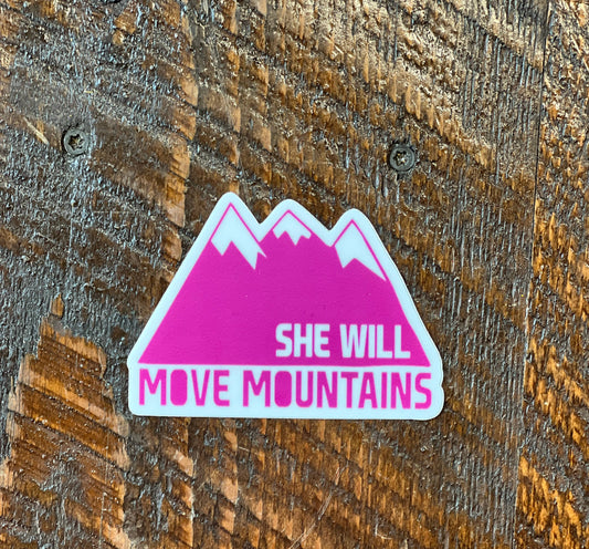 Pink mountain-shaped sticker with 'SHE WILL MOVE MOUNTAINS' text on a wooden surface