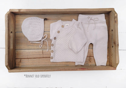 Baby outfit set with cardigan, pants, and bonnet on a wooden tray.
