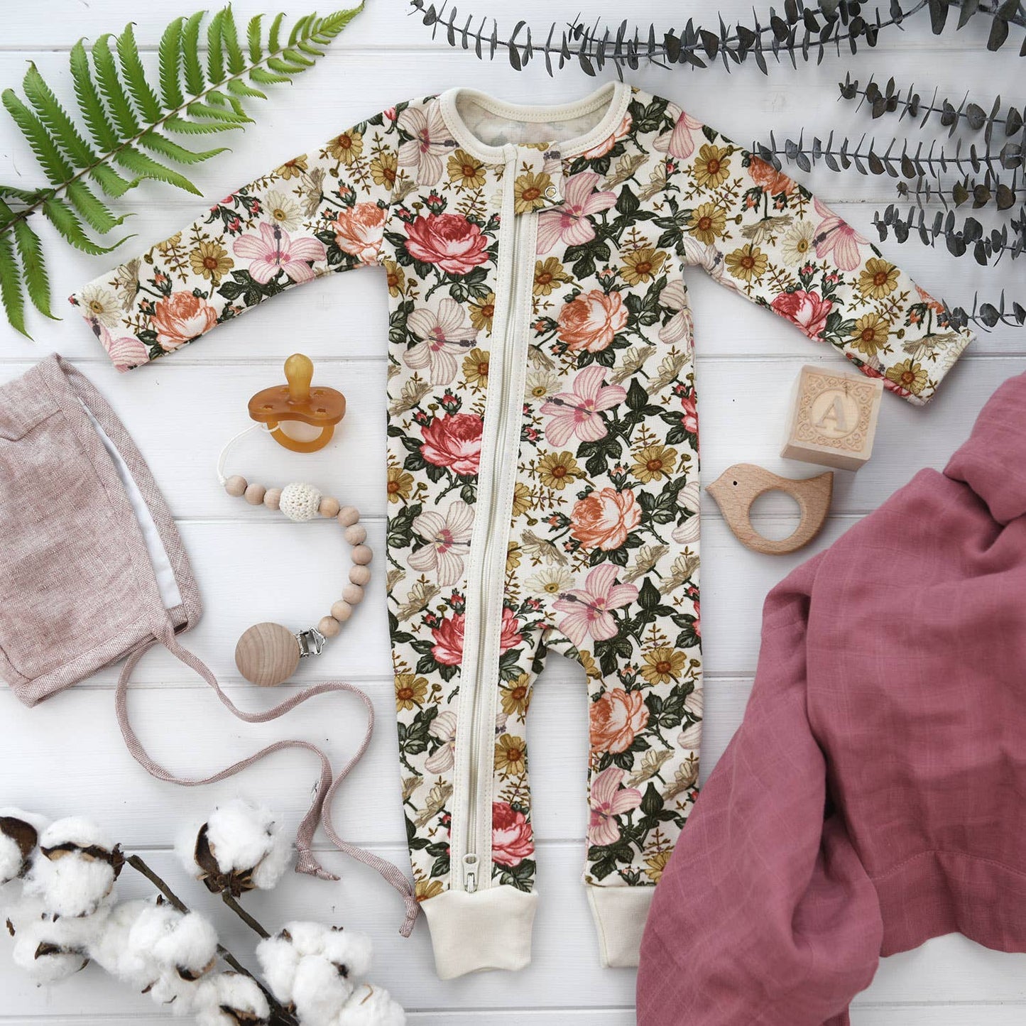 Floral-patterned baby onesie with baby accessories on a white wooden surface.