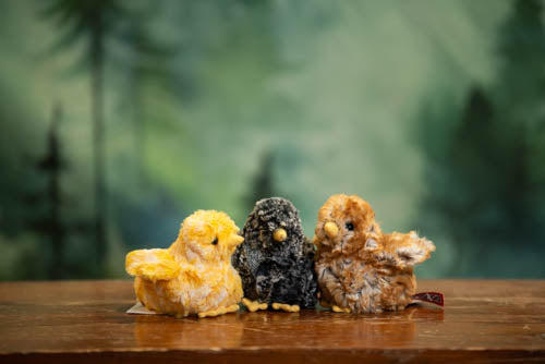 Three small bird figurines on a wooden surface with a blurred green forest background