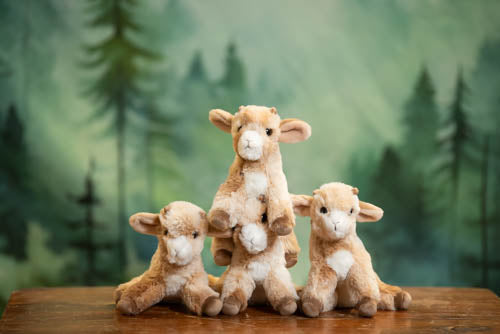 Four plush goats on a wooden surface with a forest background