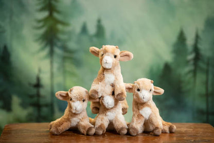 Four plush goats on a wooden surface with a forest background