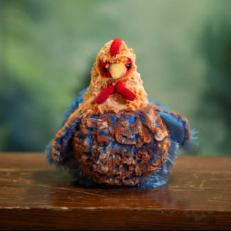 Knitted chicken toy on a wooden surface with a blurred green background
