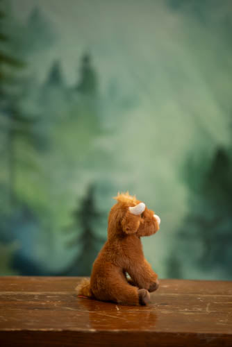 Plush toy cow sitting on a wooden surface with a forest background