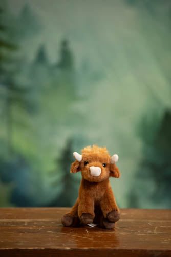 Plush toy cow on a wooden surface with a forest background