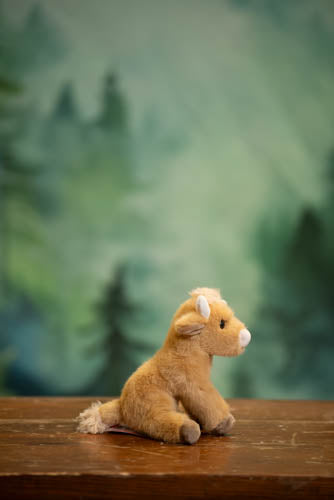 Plush toy goat on a wooden surface with a forest background