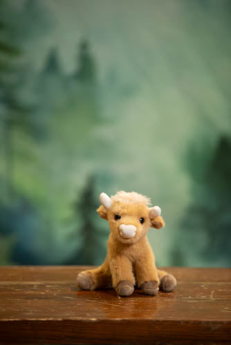 Plush toy cow on a wooden surface with a green blurred background