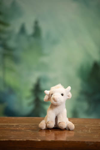 Small white plush lamb toy on a wooden surface with a blurred green forest background