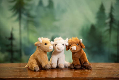 Three stuffed animal calves on a wooden surface with a forest background