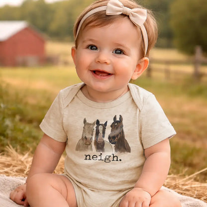 Baby wearing a onesie with horse illustrations and 'neigh' text, sitting outdoors.