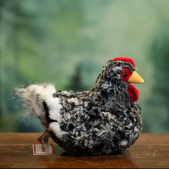 Plush toy chicken with a red comb on a wooden surface against a blurred green background