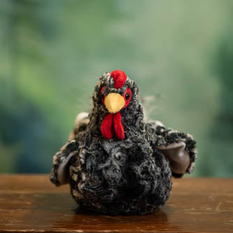 Plush toy rooster on a wooden surface with a blurred green background