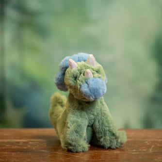 Small plush toy dragon on a wooden surface with a blurred green forest background