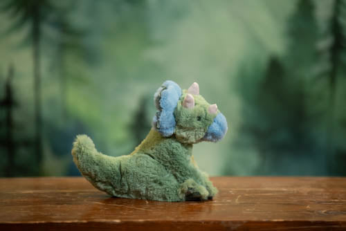 Plush toy dinosaur on a wooden surface with a blurred green background