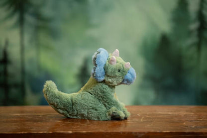 Plush toy dinosaur on a wooden surface with a blurred green background