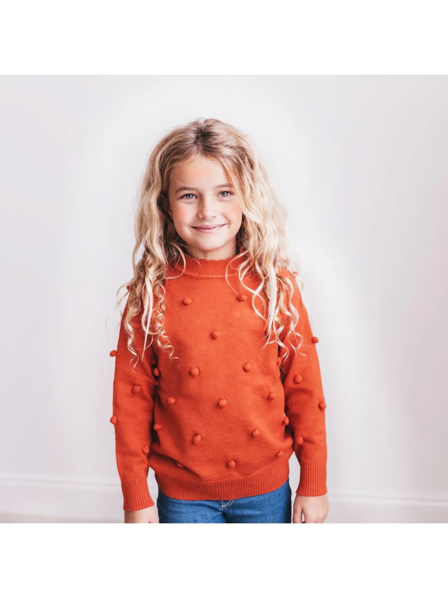 girls orange rust colored sweater with pom pom details