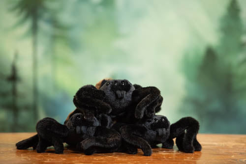 Stack of black plush toys on a wooden surface with a blurred green forest background