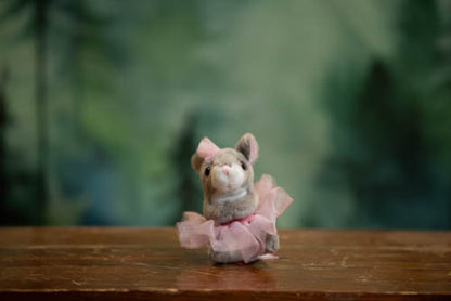 Small plush mouse toy in a pink dress on a wooden surface with a blurred green background