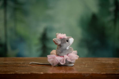 Plush toy mouse in a pink dress on a wooden surface with a blurred green background