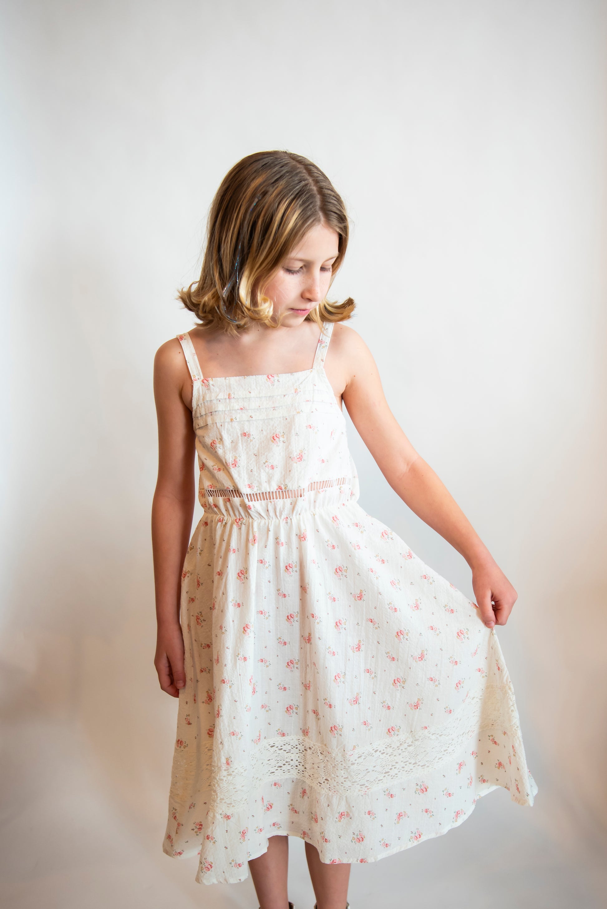 Tween wearing a white cotton sundress with delicate details and small pink flowers on it.