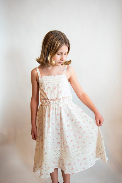 Tween wearing a white cotton sundress with delicate details and small pink flowers on it.
