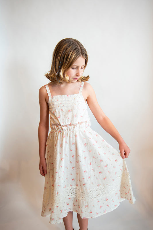 Tween wearing a white cotton sundress with delicate details and small pink flowers on it.