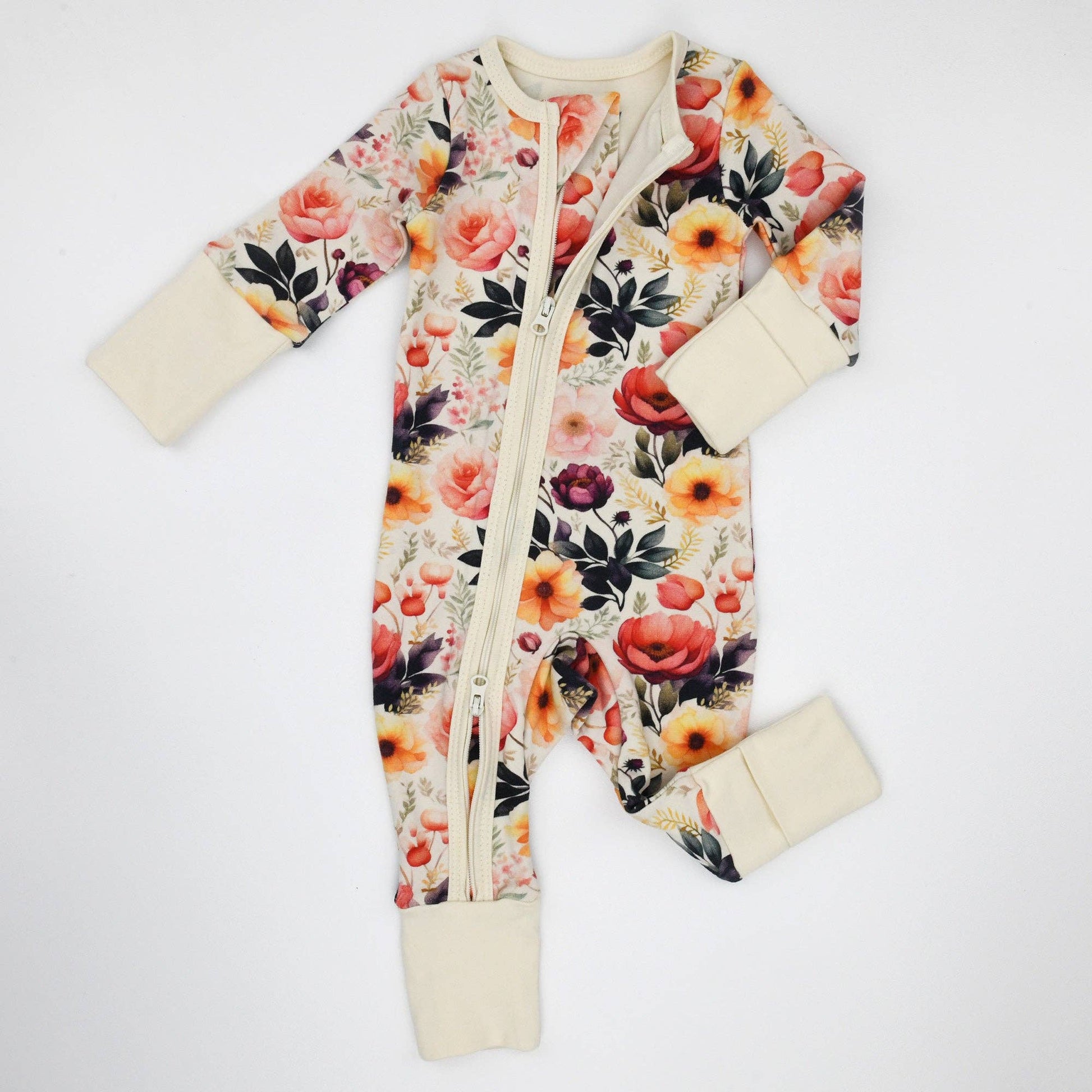 Floral patterned baby onesie with cream cuffs and footies on a white background