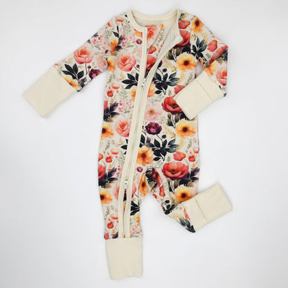 Floral patterned baby onesie with cream cuffs and footies on a white background