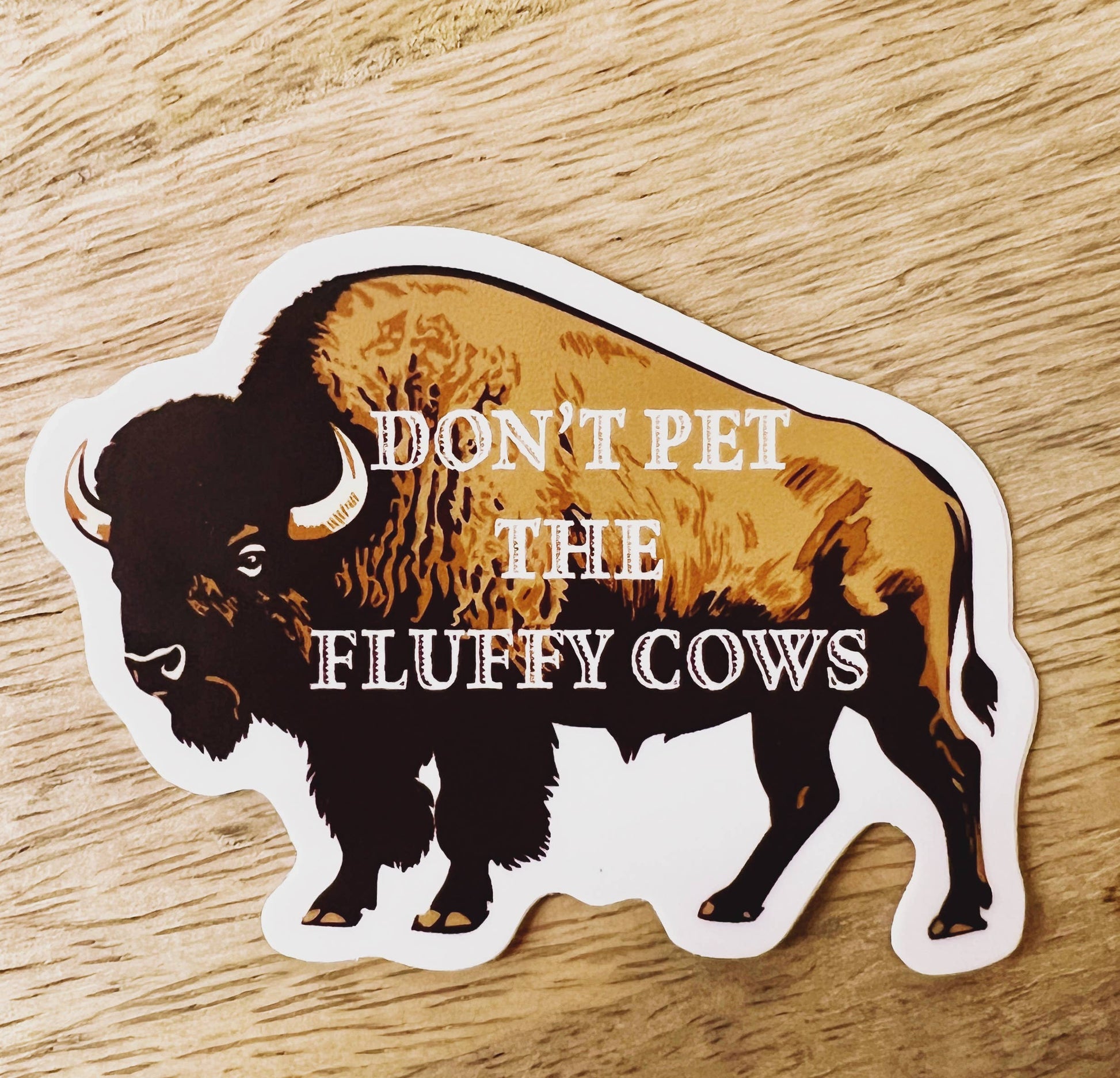 Sticker of a bison with text 'Don't pet the fluffy cows' on a wooden surface