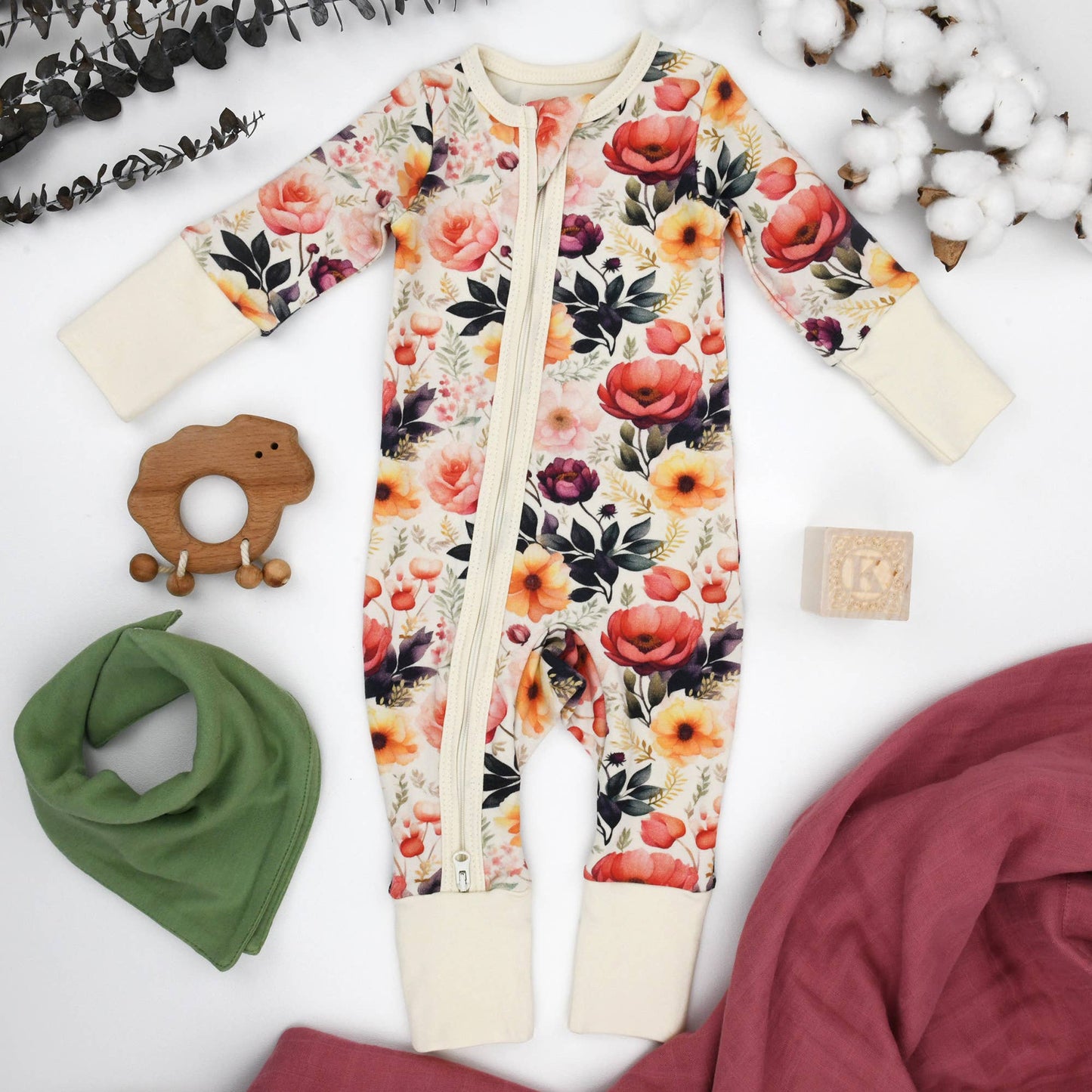 Floral-patterned baby onesie with a wooden teether and green bandana on a white background