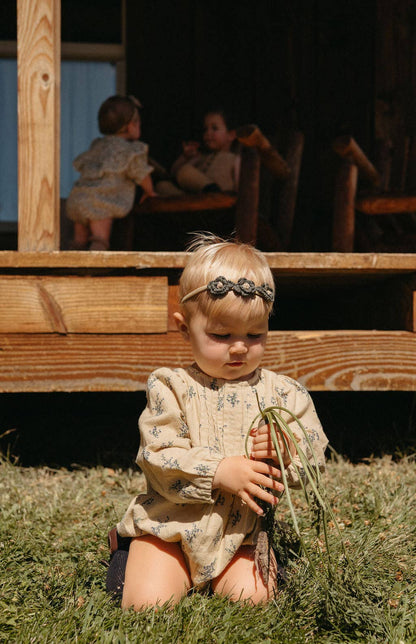 Child sitting on grass holding a plant with wooden structure and people in the background