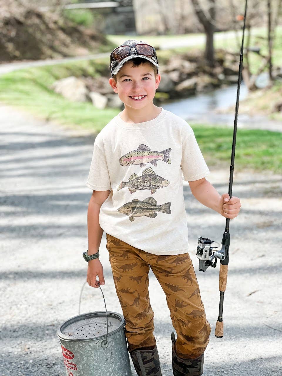Child holding a fishing rod and wearing a graphic t-shirt by a river.