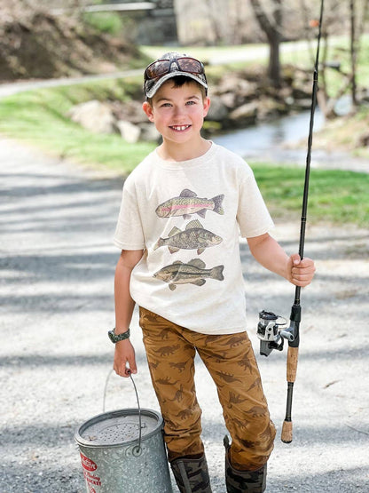 Child holding a fishing rod and wearing a graphic t-shirt by a river.