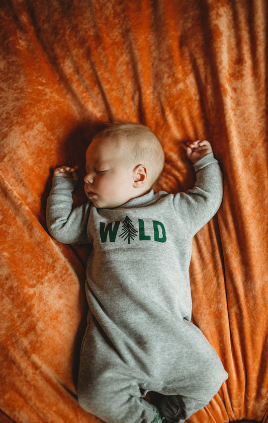 Newborn baby wearing a gray onesie with 'WILD' and tree graphics, lying on an orange blanket.