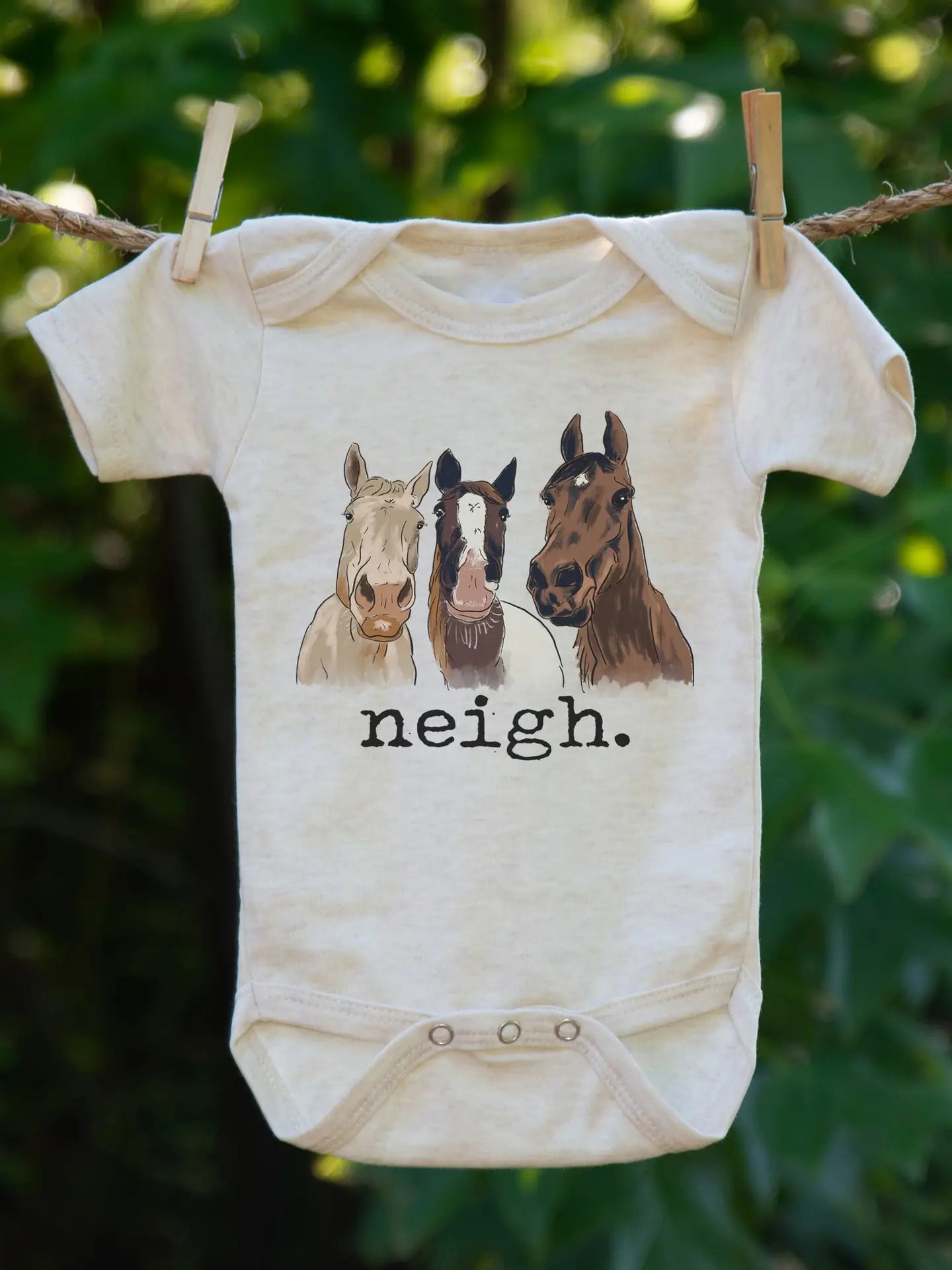 Baby onesie with horse illustrations and 'neigh' text hanging on a clothesline.