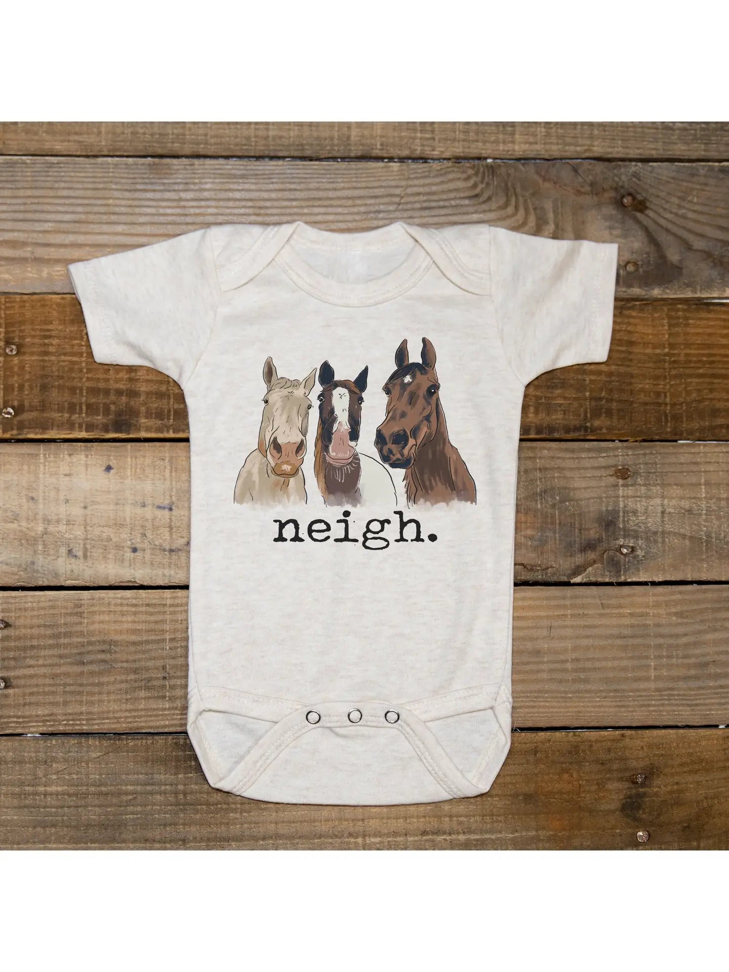 Baby onesie with horse illustrations and 'neigh' text on a wooden background