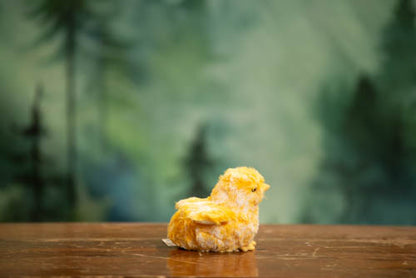 Small yellow bird figurine on a wooden surface with a blurred green forest background